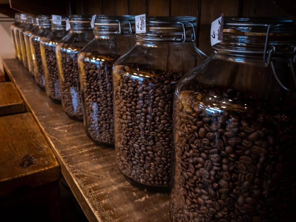 Black coffee beans glass jar packaging package on wood stand at caffe shop background. Freshly roasted cafe bean on house bottle.