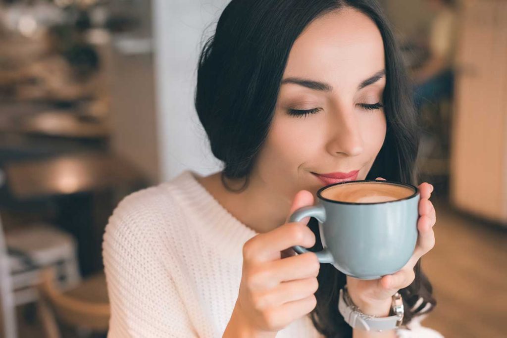 Woman smelling a cappuccino in a nice mug.