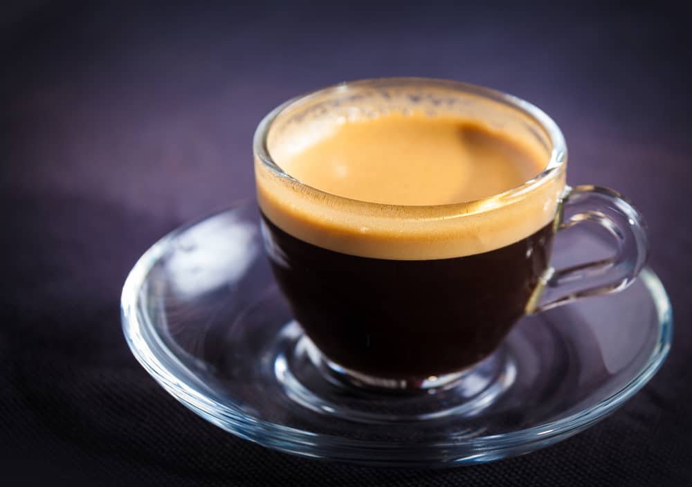 Closeup of a cup of black coffee in a clear cup with a lot of crema.