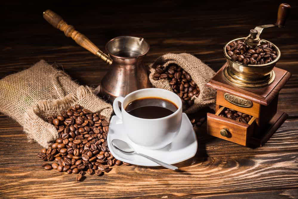 Cup of coffee net to an old grinder and coffee beans.