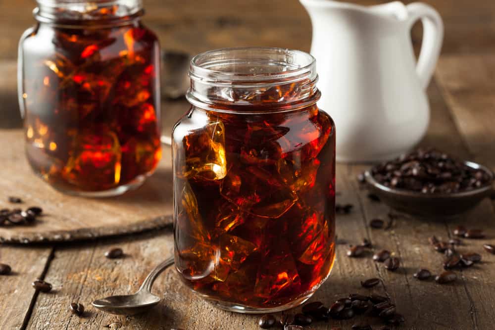 Two cold brews in mason jars with ice on a wooden table.