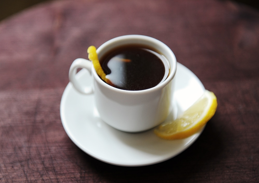Espresso romano coffee with lemon in a white cup on a dark wooden rustic table closeup