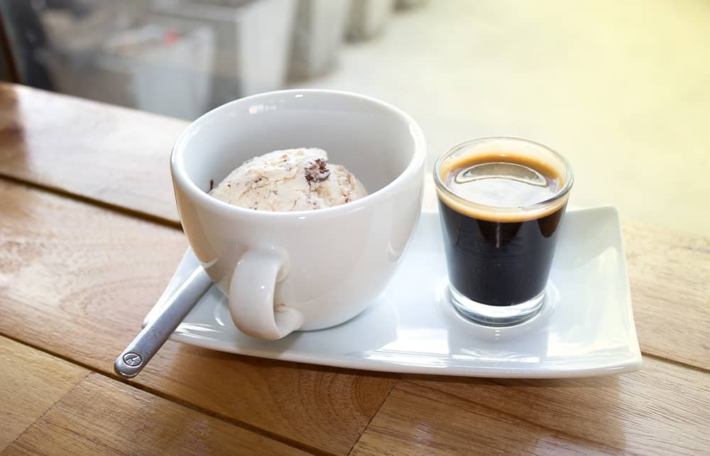 A rectangular dish with a cappuccino cup on the left containing ice cream and a shot of espresso to the right of it