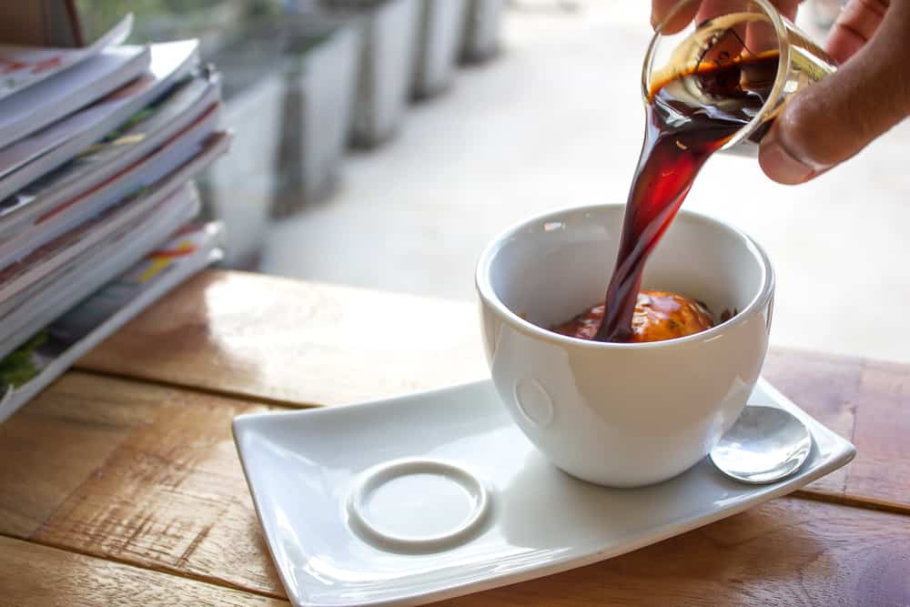 A cappuccino mug containing ice cream with a shot of coffee being poured onto it