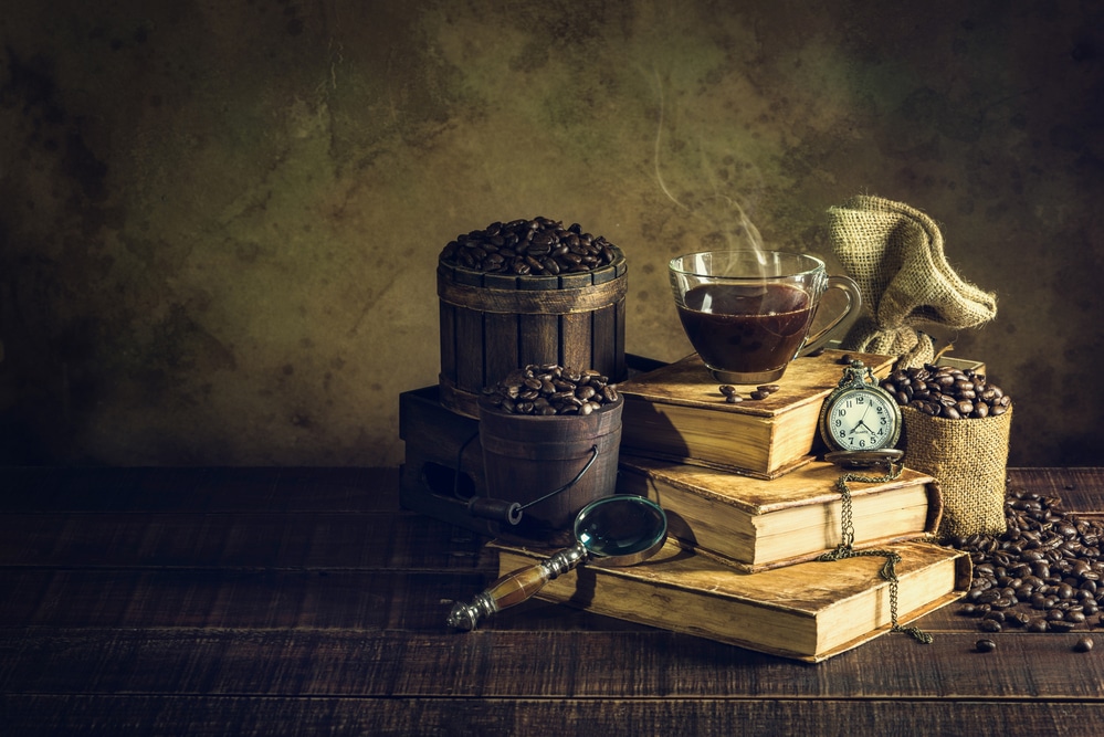 Coffee in cup glass on old books and clock vintage on aged wood floor.