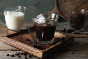 Glass of delicious iced coffee, milk and beans on wooden table
