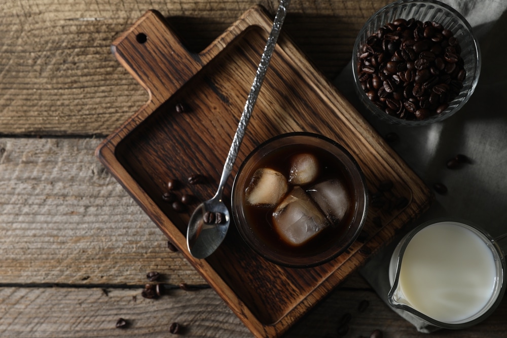 Delicious iced coffee, milk and beans on wooden table, flat lay