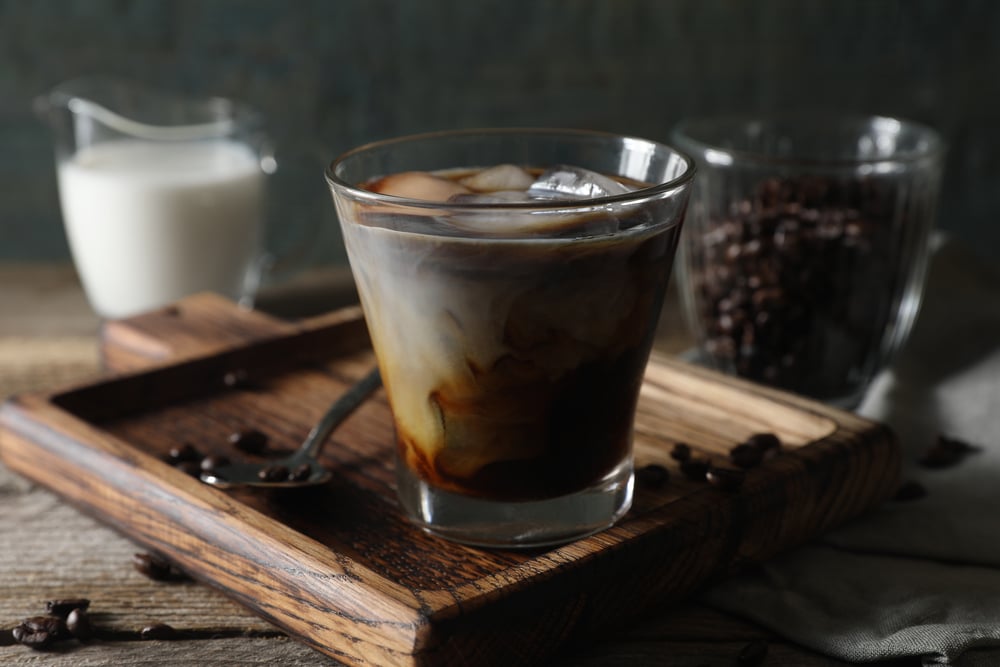 Glass of delicious iced coffee with milk and beans on wooden table