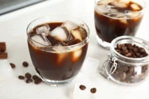 Glass of coffee drink with ice cubes and beans in jar on table